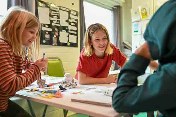 Girl leans over table to talk to boy at homeschool coop.