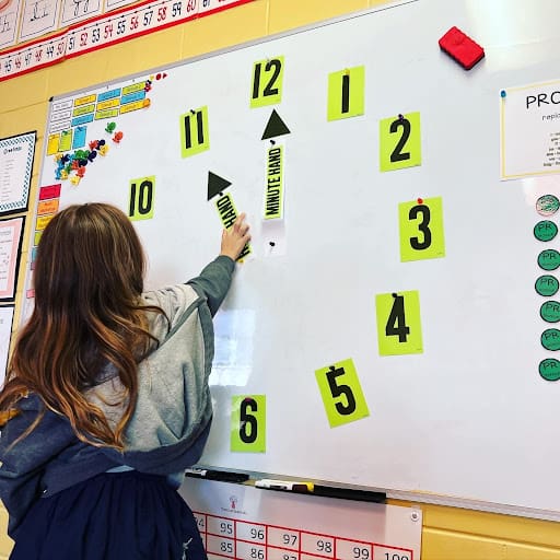 Elementary girl works with numbers at clock on board