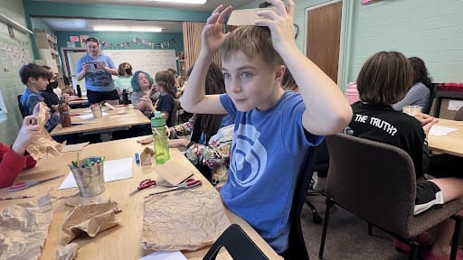Boy puts cardboard on head while working language arts project.