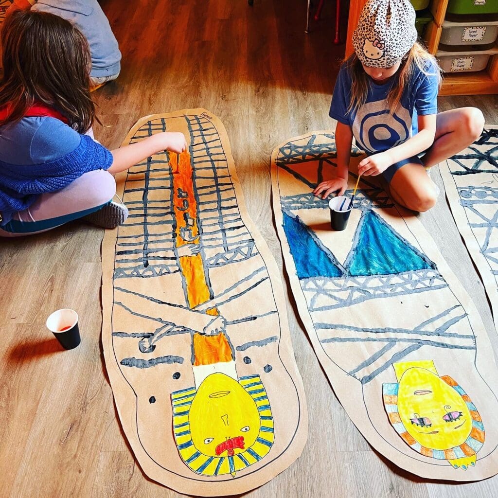 Second grade students color Egyptian project on the floor at non-traditional school.